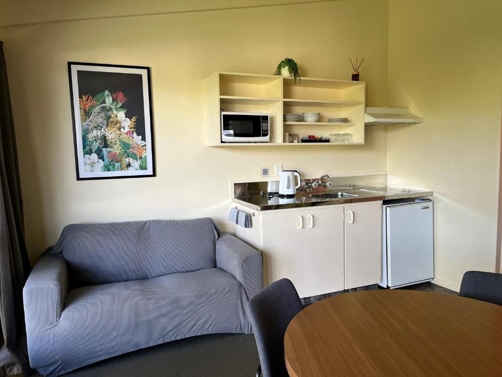 Ein kompakter Wohnraum mit Küchenzeile, einer Couch, einem Esstisch und einem floralen Bild in einem Rahmen an der Wand.