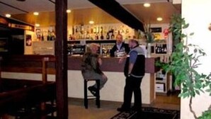 Zona de bar con mostrador, taburetes y estanterías llenas de botellas.