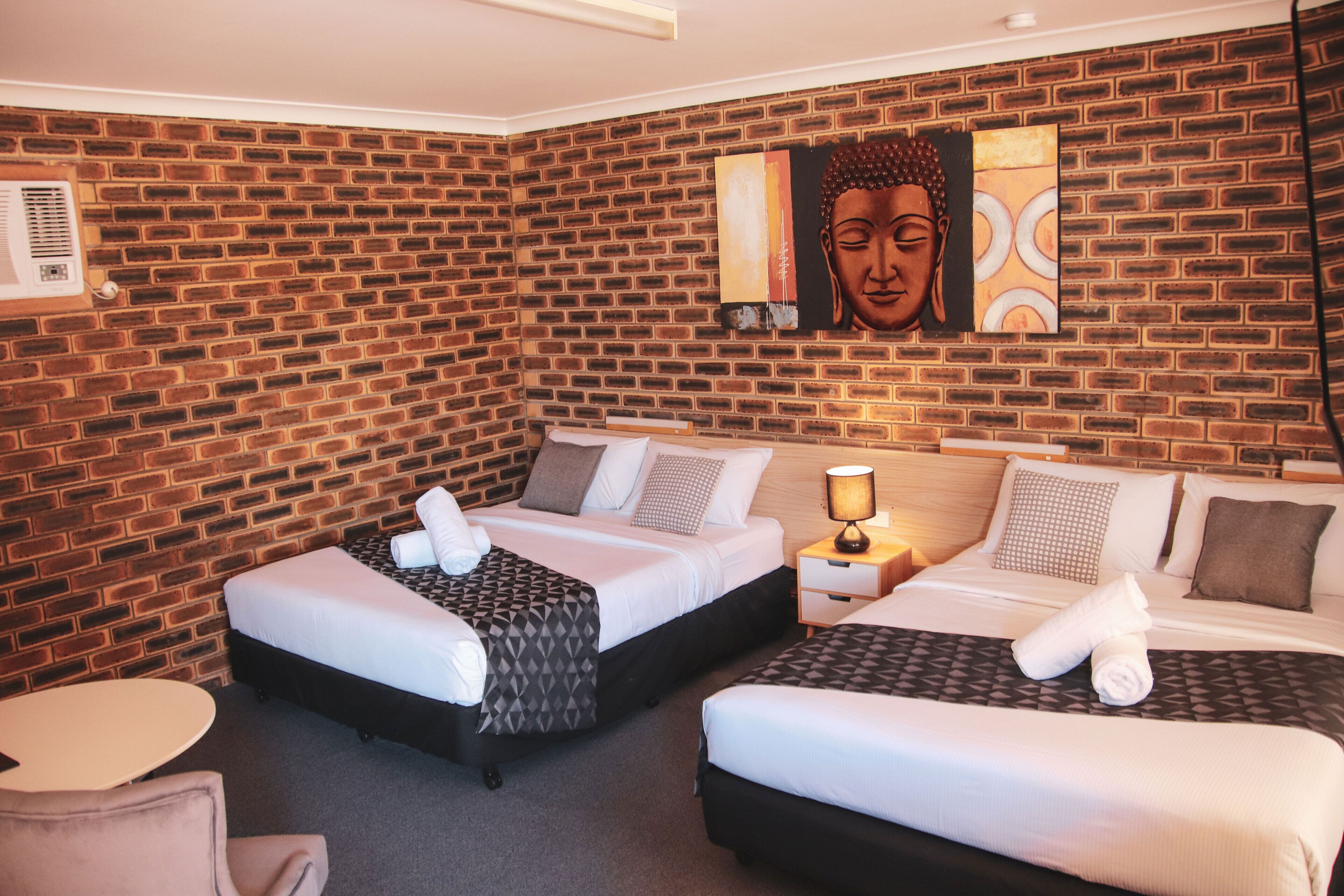 A hotel room with two beds, a brick wall, and artwork.