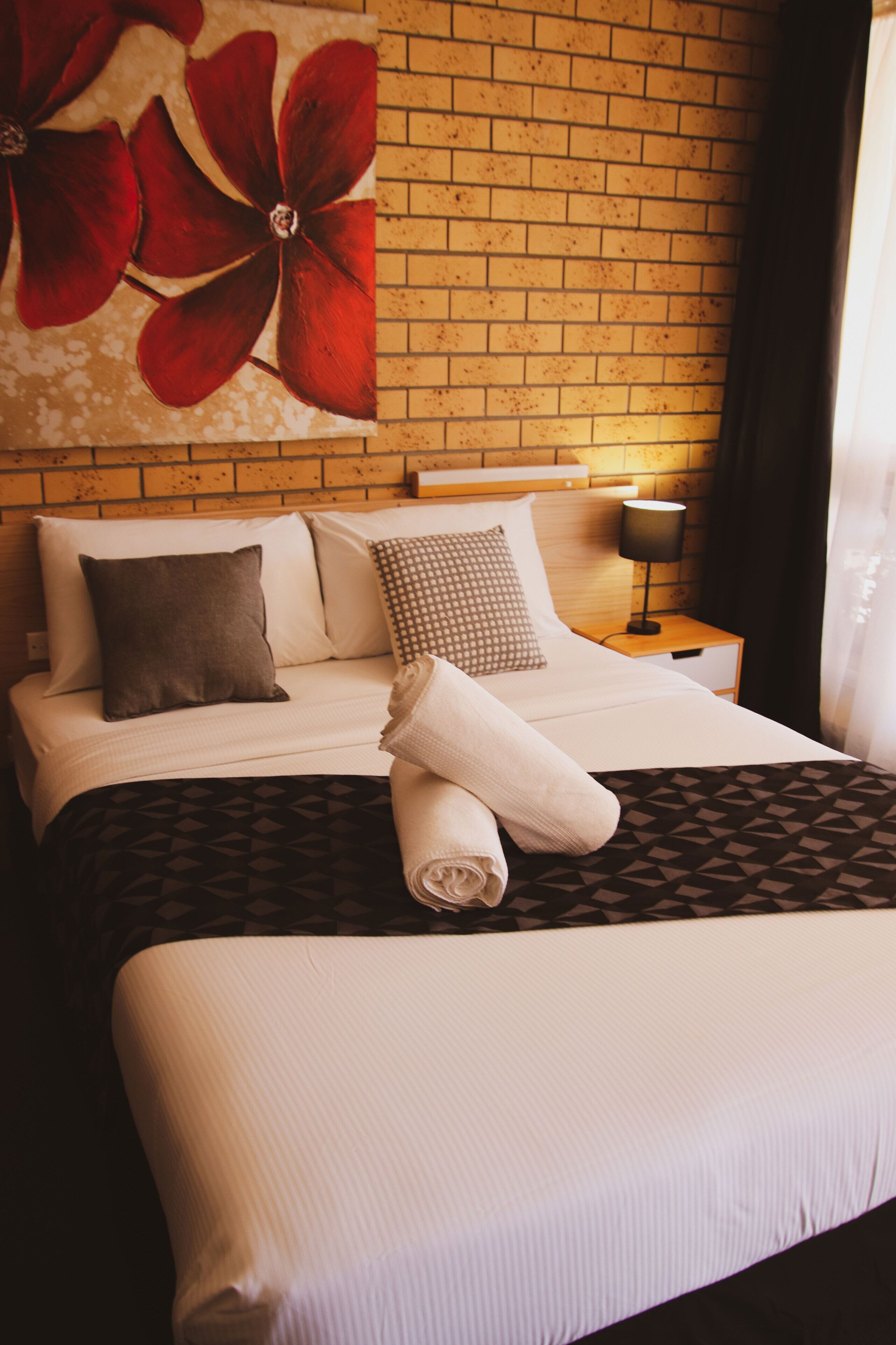 A neatly made bed with a patterned bedspread, a pillow, and a rolled towel.