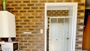 A compact room with a brick-patterned wall, a microwave, a small white desk, and a door leading to a shower area. - Squatters Homestead Motel (Casino)