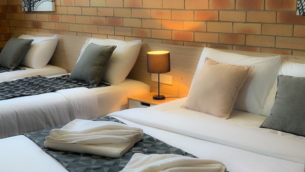 A hotel room with two beds, a brick wall, and a nightstand with a lamp. - Squatters Homestead Motel (Casino)