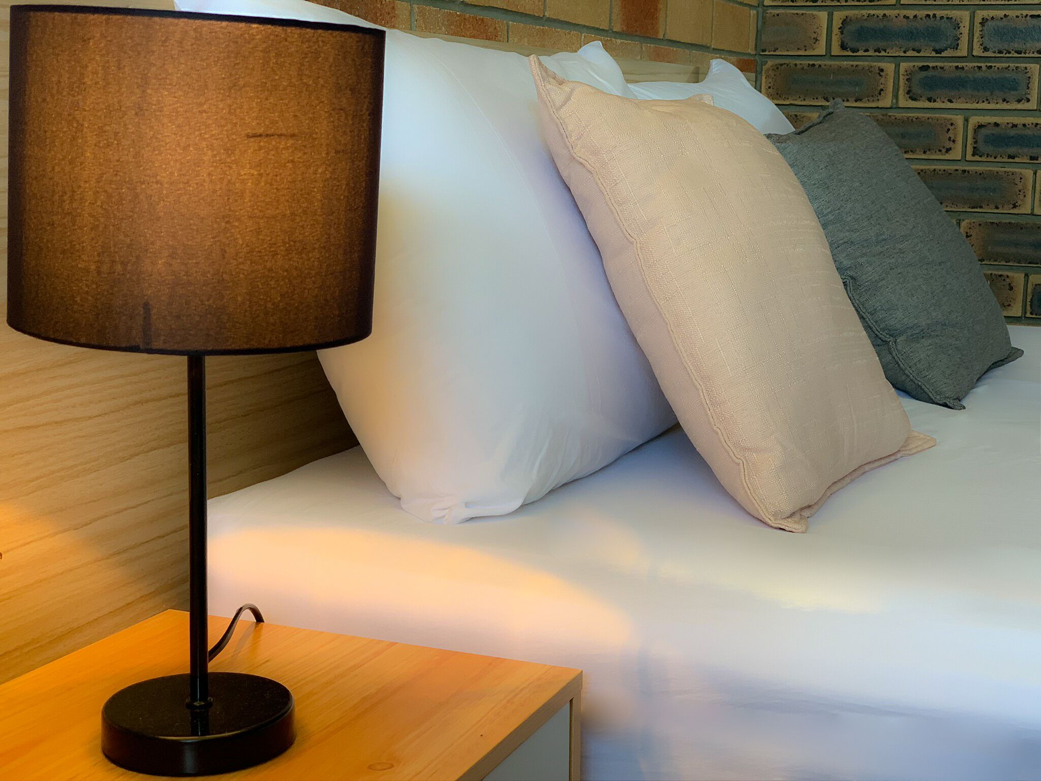 A bed with white and grey pillows, a wooden bedside table, and a black lamp.