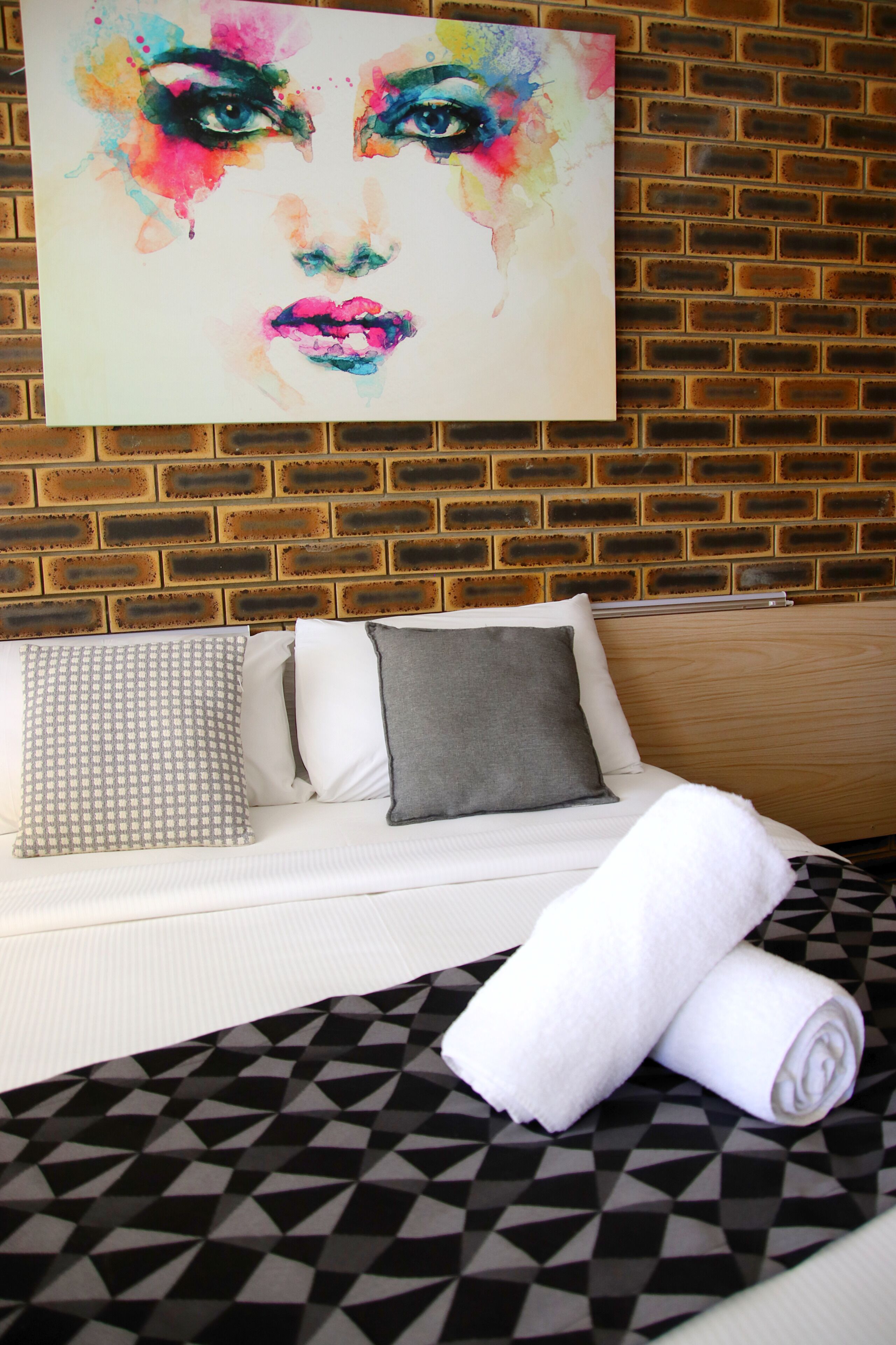 A hotel room with a brick wall, a white sofa with patterned pillows, and a black and white patterned bedspread.