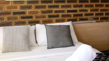 A hotel room with a brick wall, a white sofa with patterned pillows, and a black and white patterned bedspread.