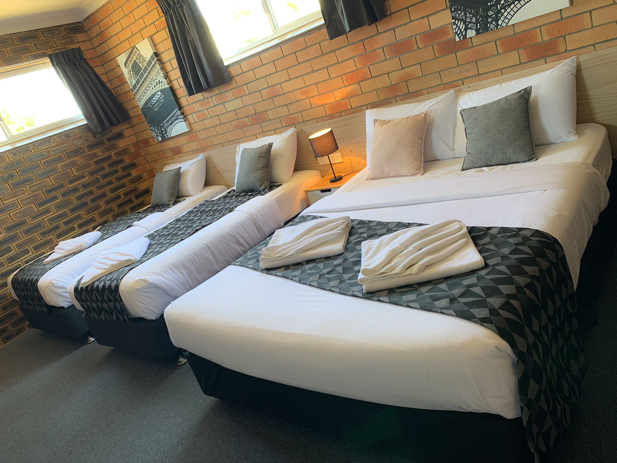A hotel room with two beds, a brick wall, and a window with curtains.