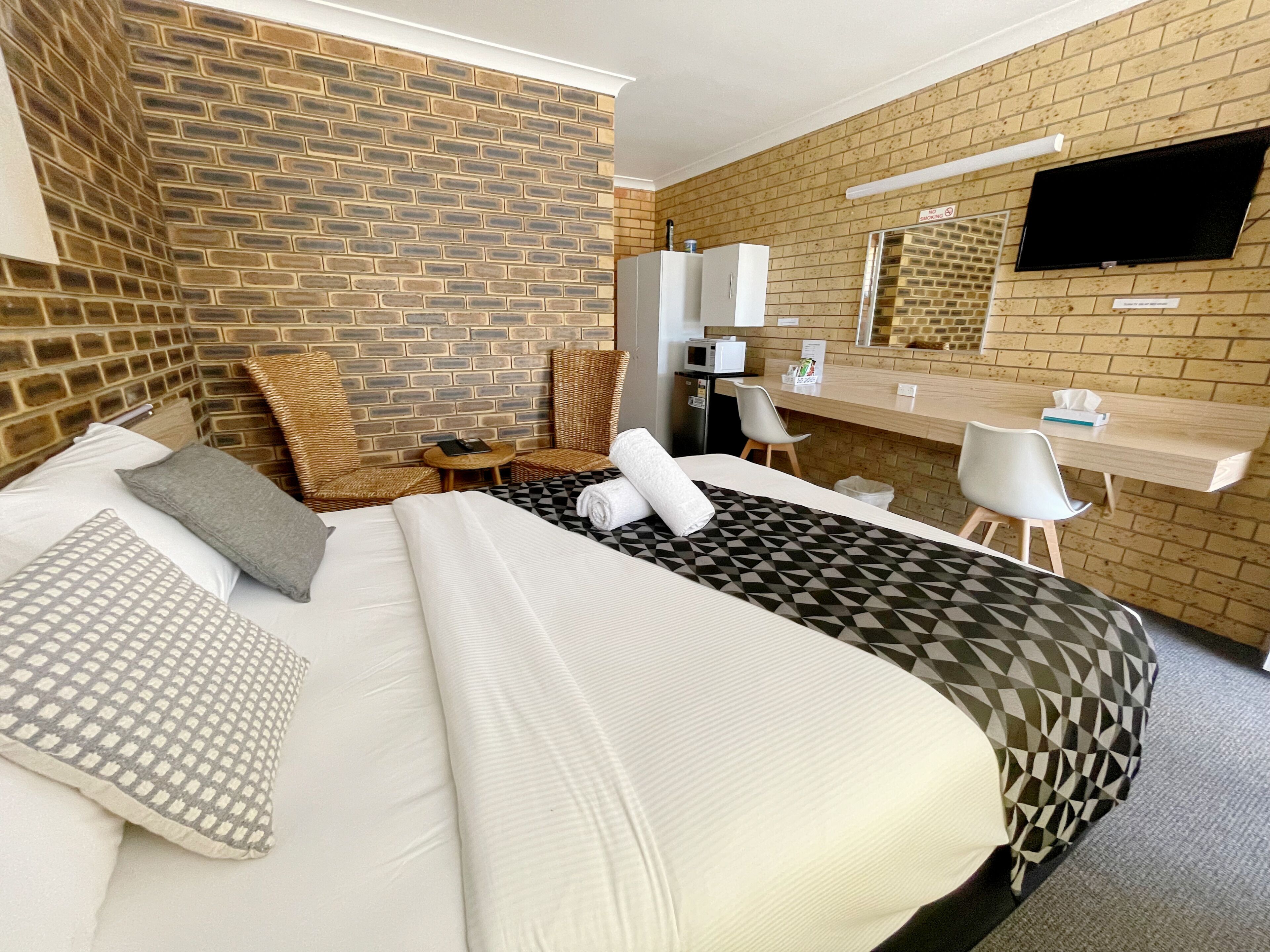Une chambre d’hôtel avec un mur en briques, un lit recouvert d’une courtepointe à motifs géométriques, un téléviseur à écran plat fixé au mur et un petit bureau avec une chaise.