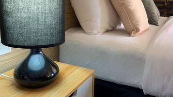 A neatly made bed with pillows, a bedside table with a lamp, and a brick-patterned wall.
