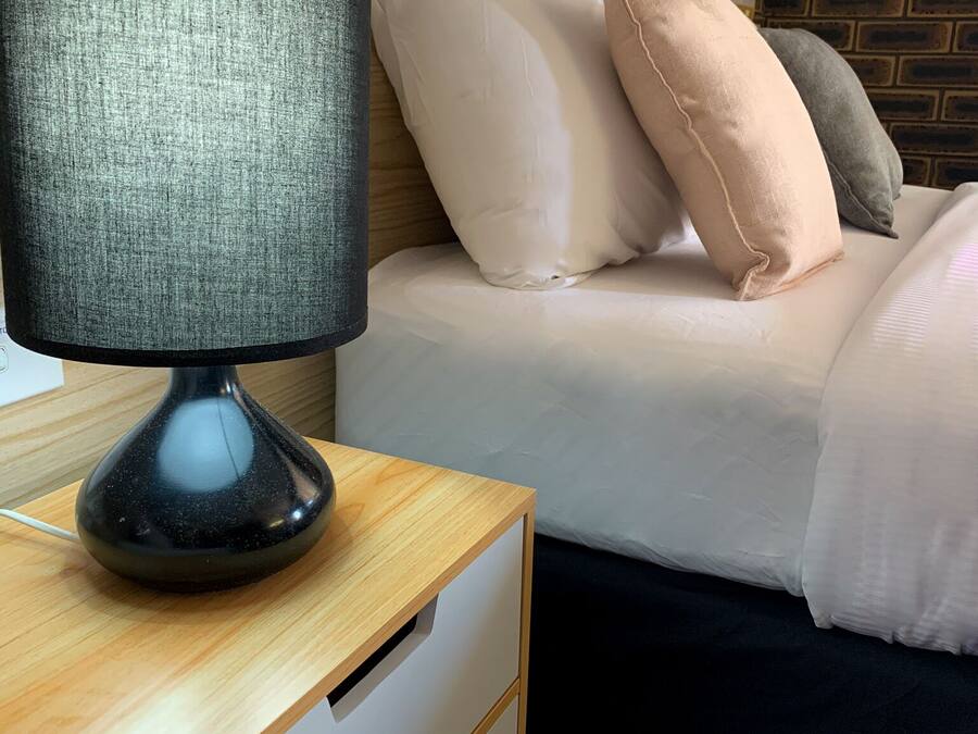 A neatly made bed with pillows, a bedside table with a lamp, and a brick-patterned wall.