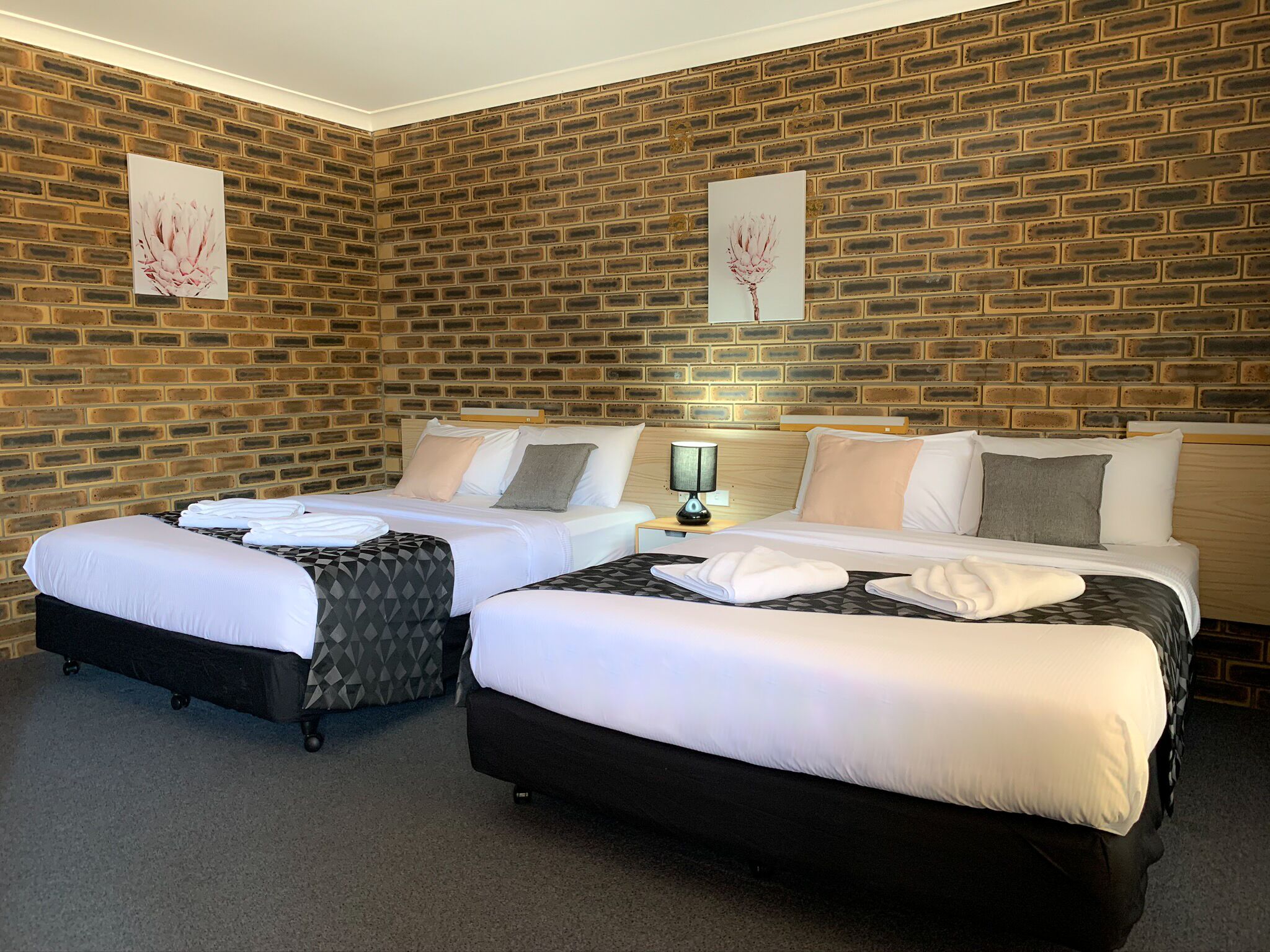 Habitación de hotel con dos camas, una pared de ladrillo y obras de arte.
