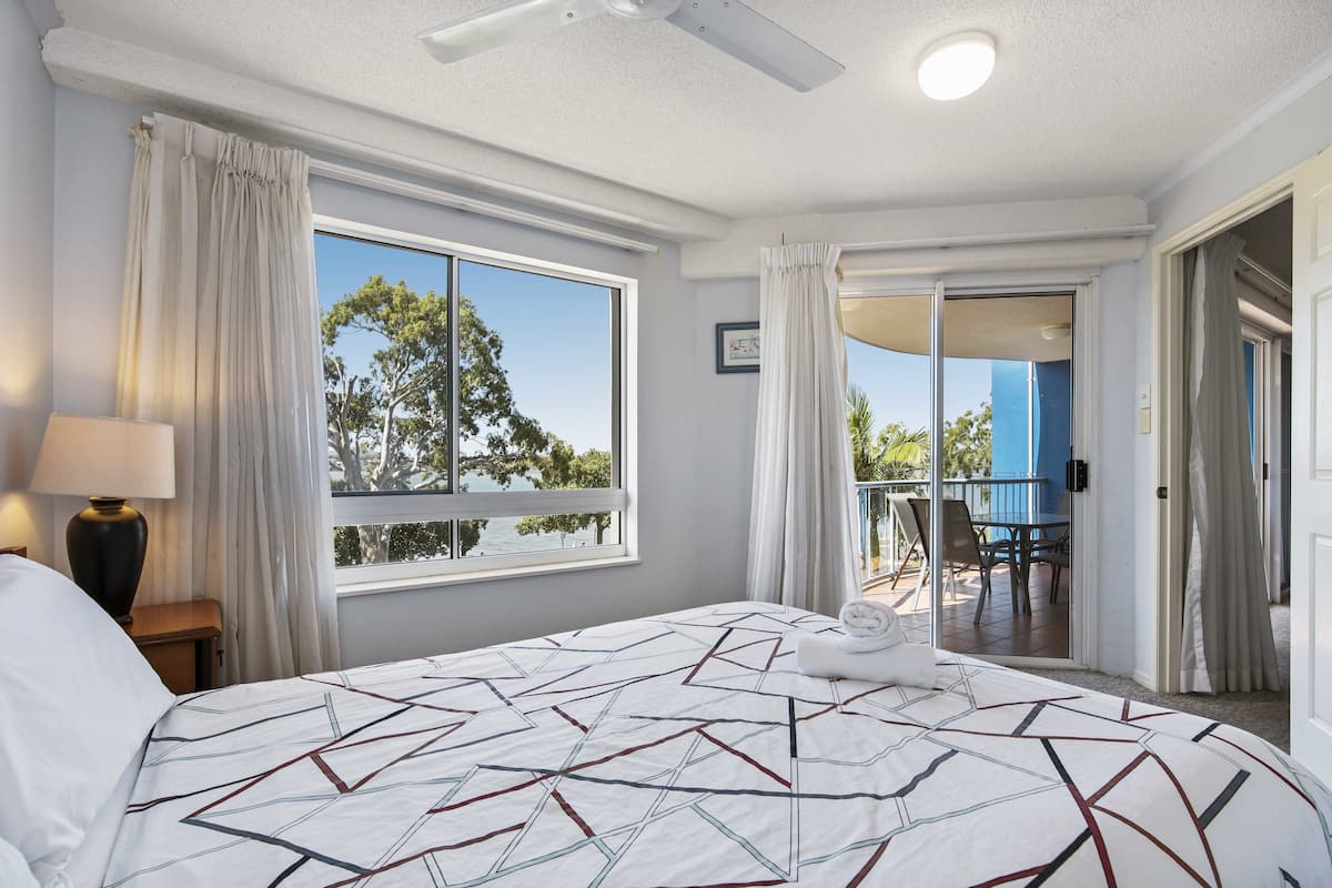 A hotel room with a large bed, a ceiling fan, a window with curtains, and a view of the outside.