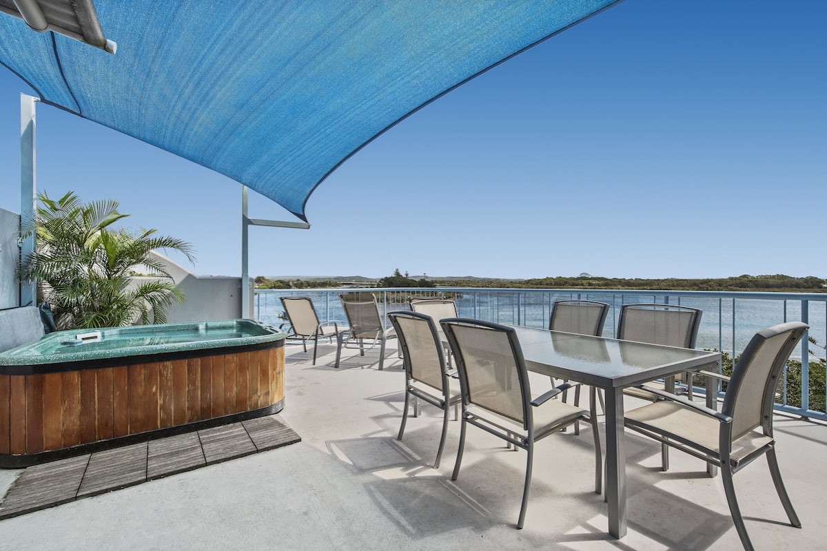An outdoor patio with a hot tub, seating area, and a view of the sea.