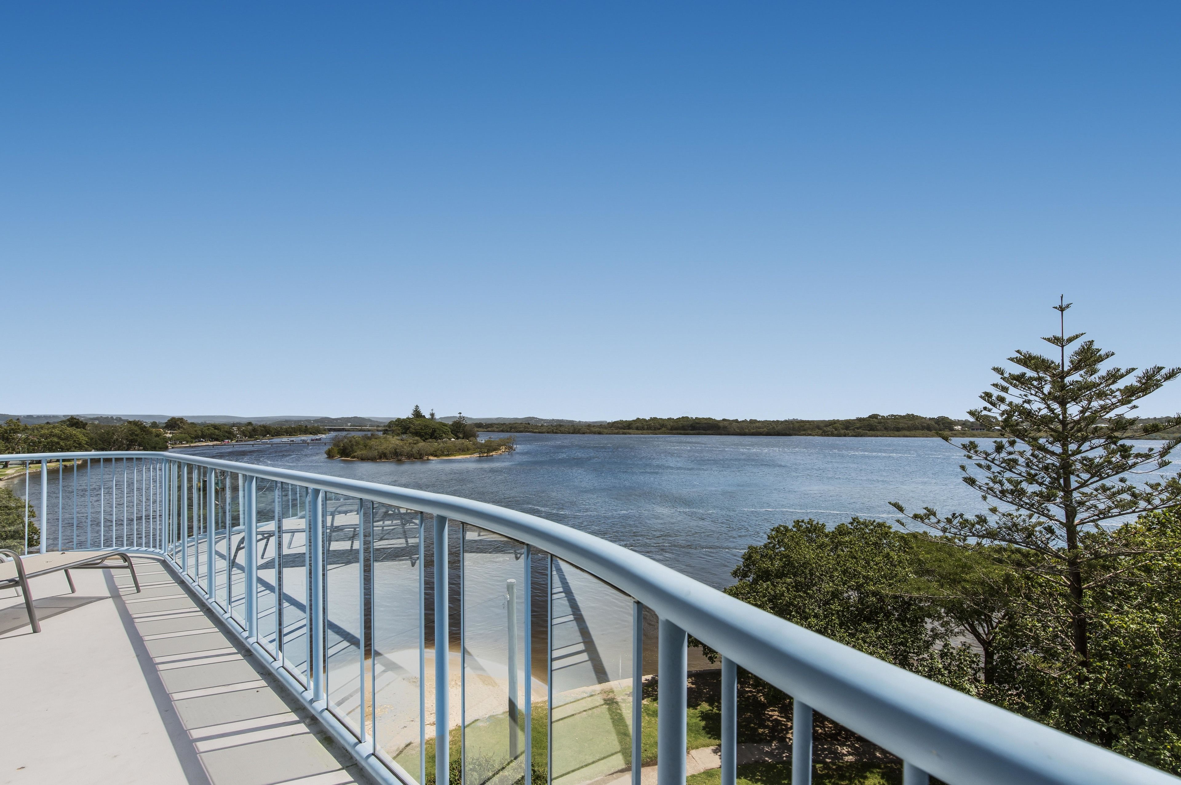 A clear view of a river from a bridge with a railing, surrounded by greenery.