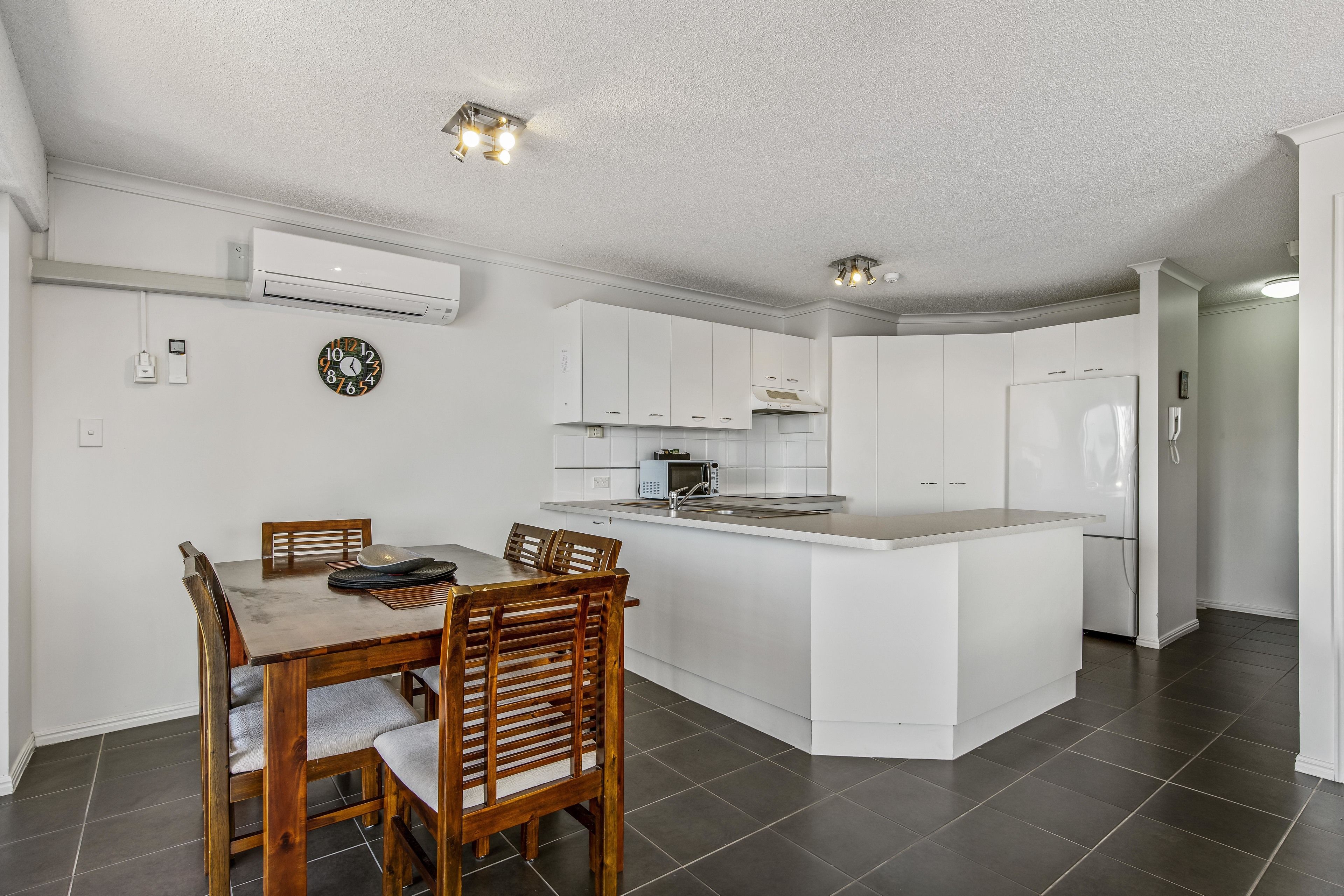 A modern kitchen with white cabinets, a central island, and a dining area with wooden chairs.