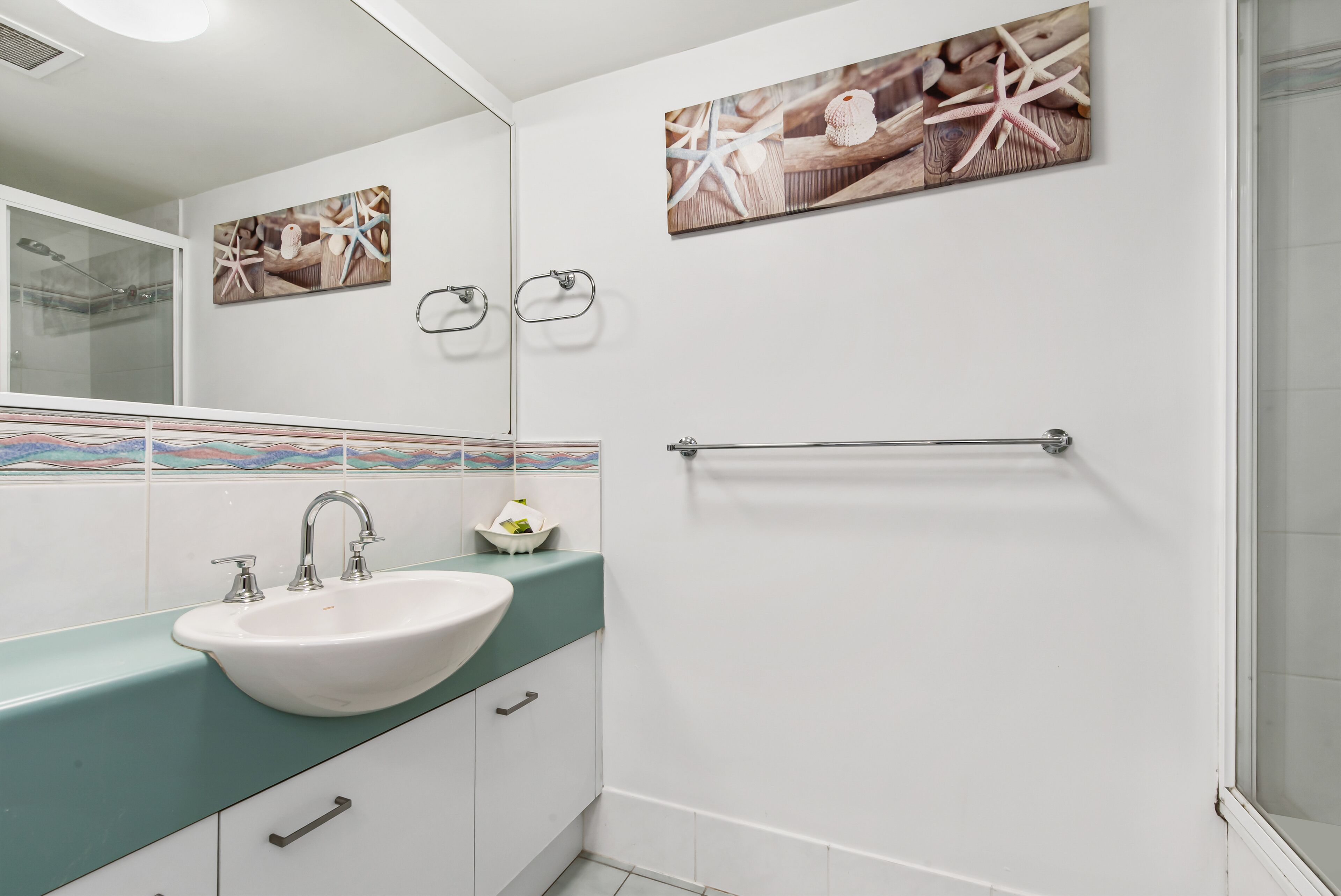 Casa de banho com lavatório branco, bancada verde-água e cabine de duche em vidro.