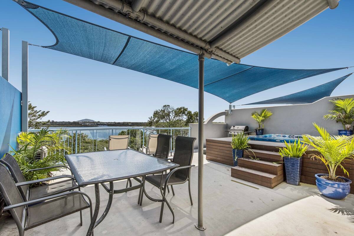 A rooftop patio with a table and chairs, a hot tub, and potted plants.