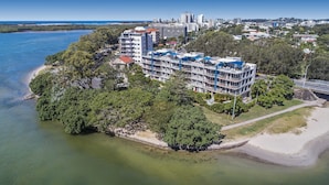 An aerial view of a coastal hotel with multiple floors, surrounded by lush greenery and a beach. - Reflections Holiday Apartments (Maroochydore)