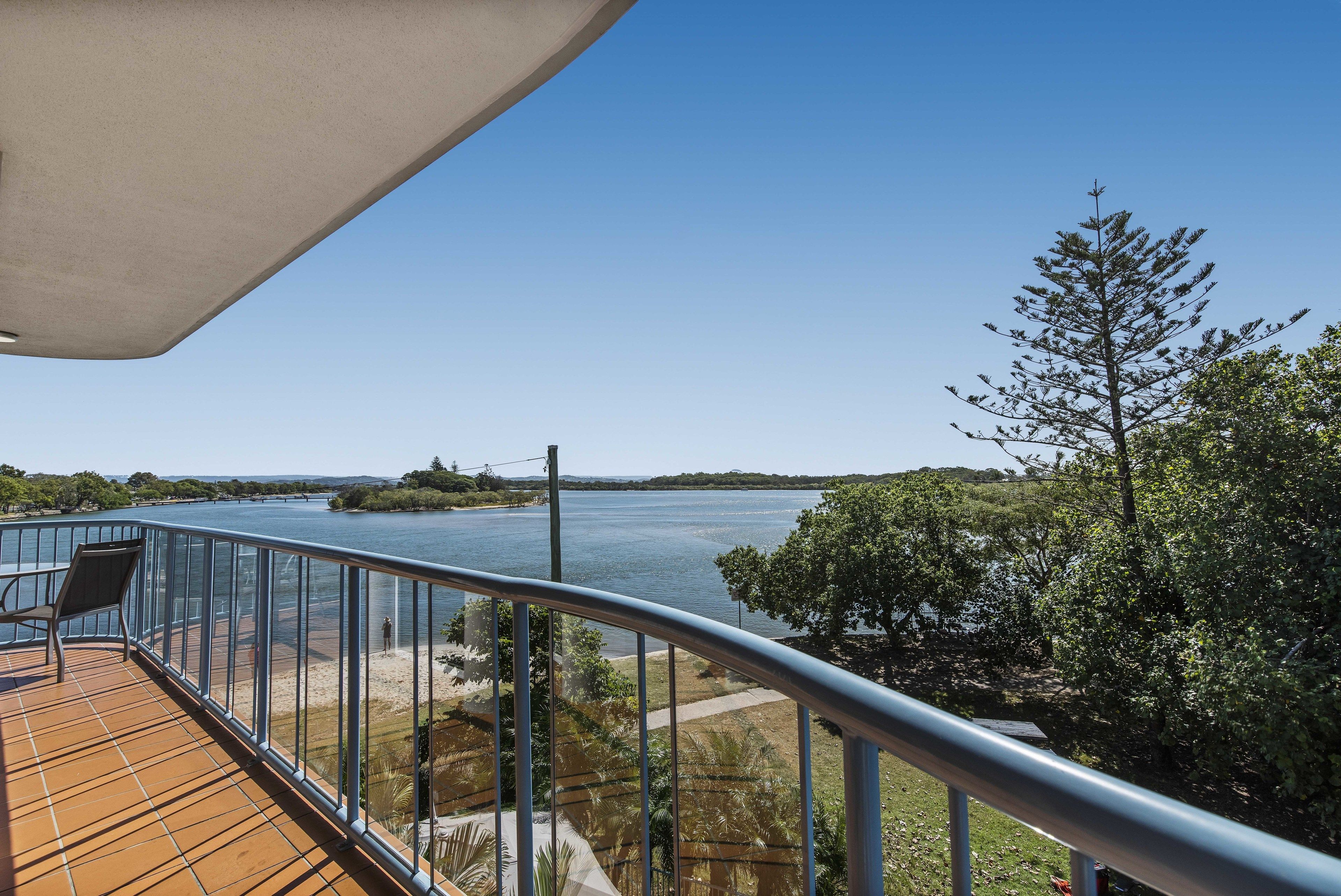 A balcony with a view of a river and distant land, metal railing, and a chair.