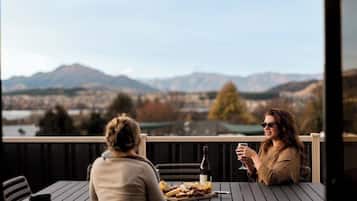 Two people seated at a table with a bottle of wine and a plate of food, overlooking a mountainous landscape.