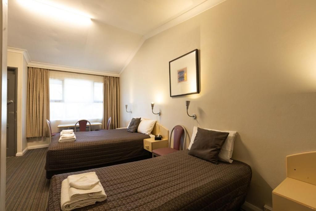 A hotel room with two beds, a desk, a chair, and a framed picture on the wall.
