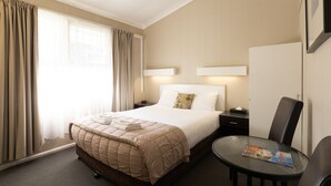 Una habitación de hotel con cama, mesitas de noche, una silla, una mesa redonda y una ventana con cortinas.