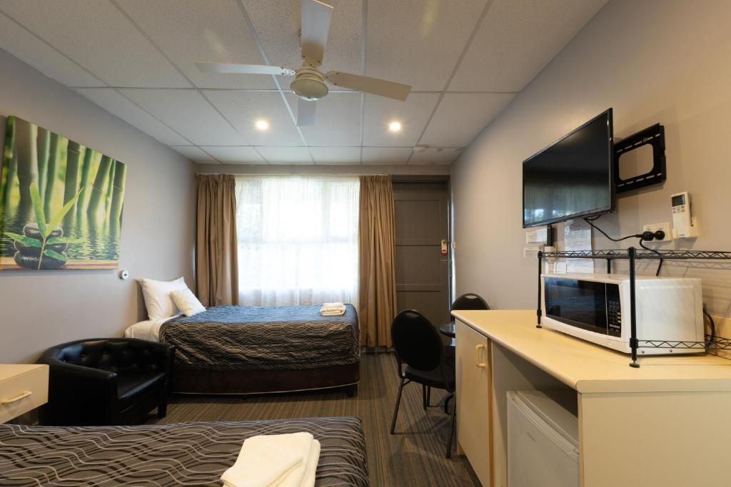 A hotel room with a bed, a desk, a chair, a television, and a microwave.