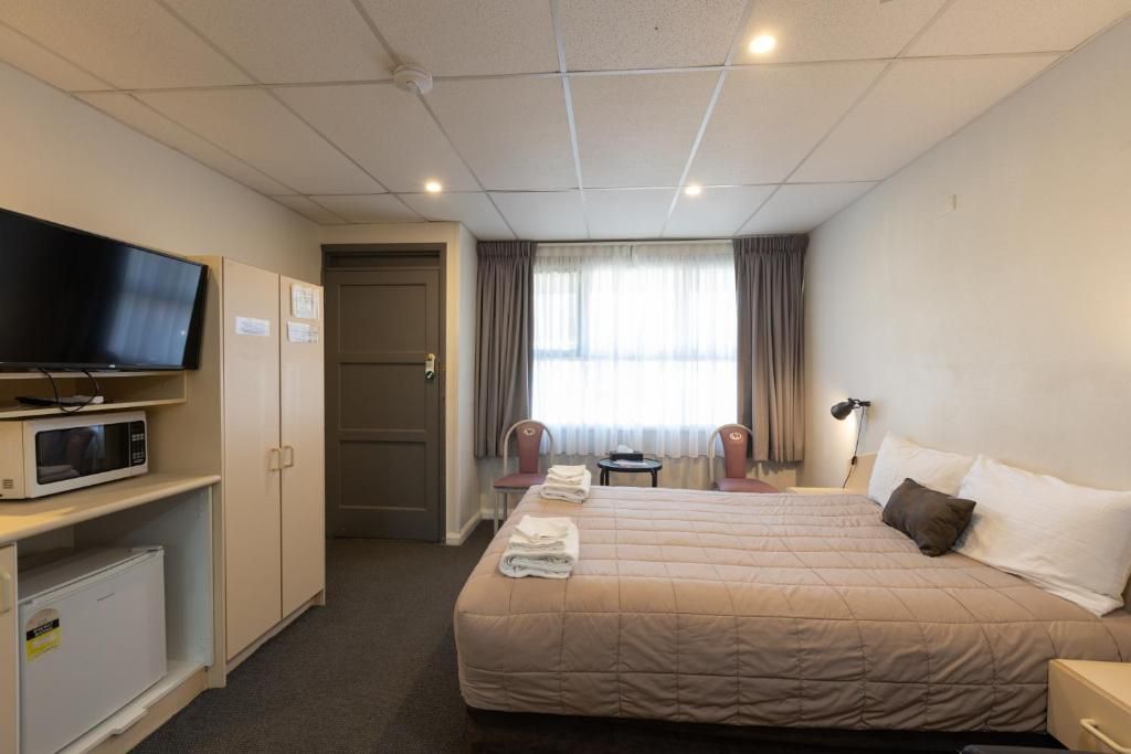 Quarto de hotel com cama, televisão, micro-ondas, frigorífico, secretária e cadeira.