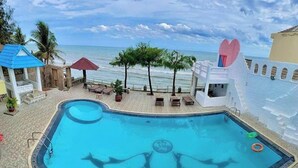 Zona de piscina con vista al océano, una decoración con forma de corazón y un pequeño edificio con techo azul.