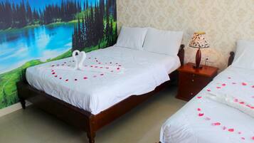 A double bed with white linens and rose petals, a nightstand with a lamp, and a forest mural on the wall.