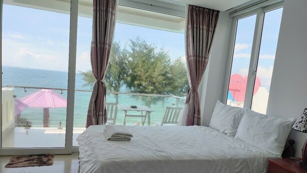 Un dormitorio con una cama grande, vista al océano y un balcón con mesa y sillas.