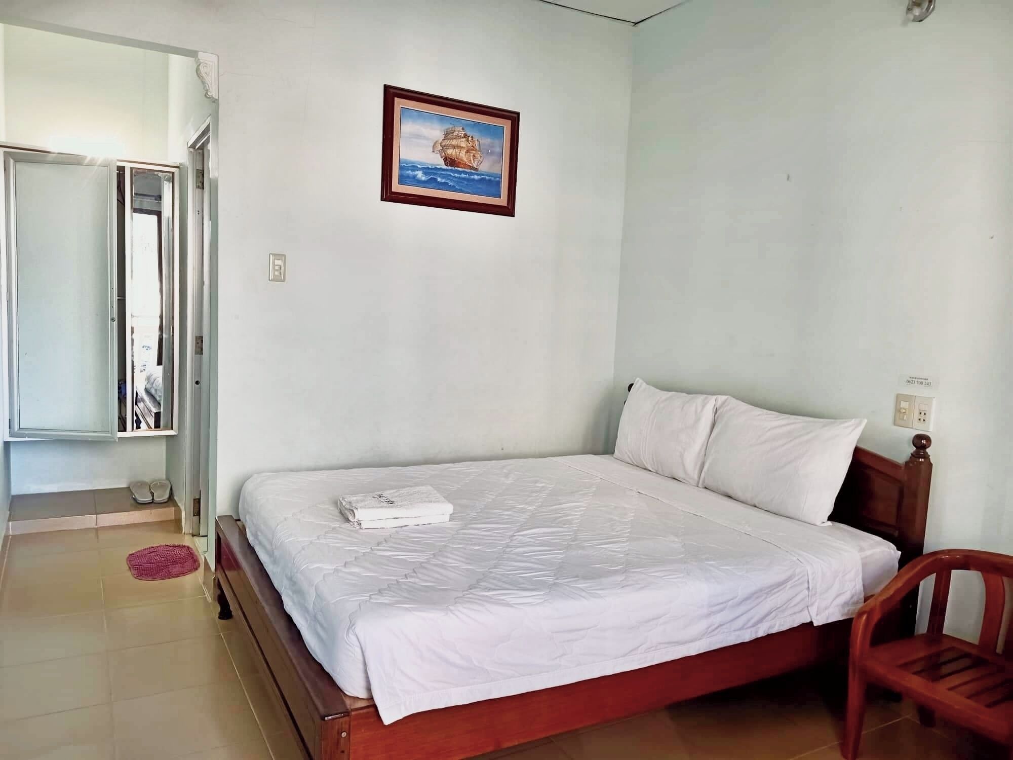 Un dormitorio con una cama, cabecera de madera, una sola almohada blanca, un cuadro en la pared y una silla roja.