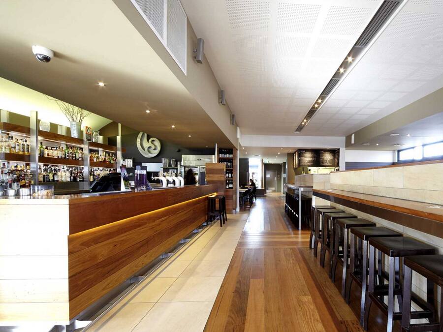 Un bar moderno con mostradores de madera, una variedad de botellas de licor y una barra larga con taburetes.