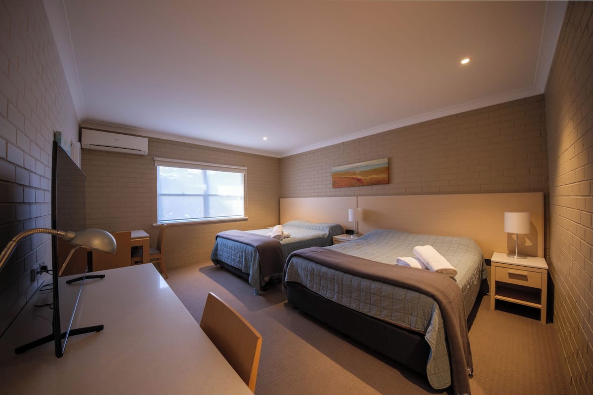 A hotel room with two beds, a desk, a chair, a lamp, and a window.