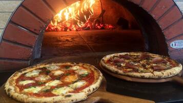 Dos pizzas en un horno de ladrillo con llamas visibles.
