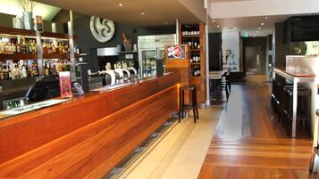 A bar area with a wooden counter, bar stools, and a wine rack in the background.
