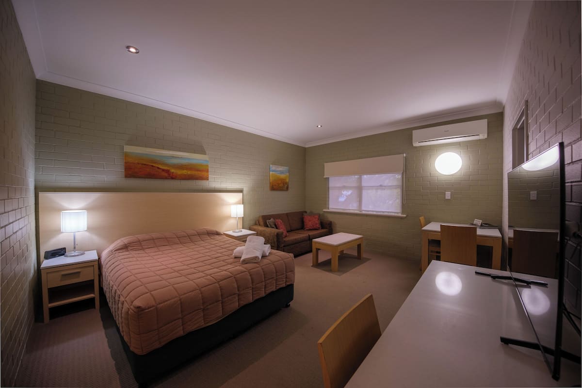 A hotel room with a bed, a desk, a chair, a sofa, and two paintings on the wall.