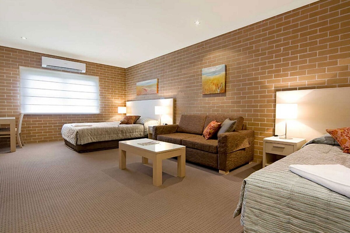 A hotel room with two beds, a sofa, a small table, and a brick wall.