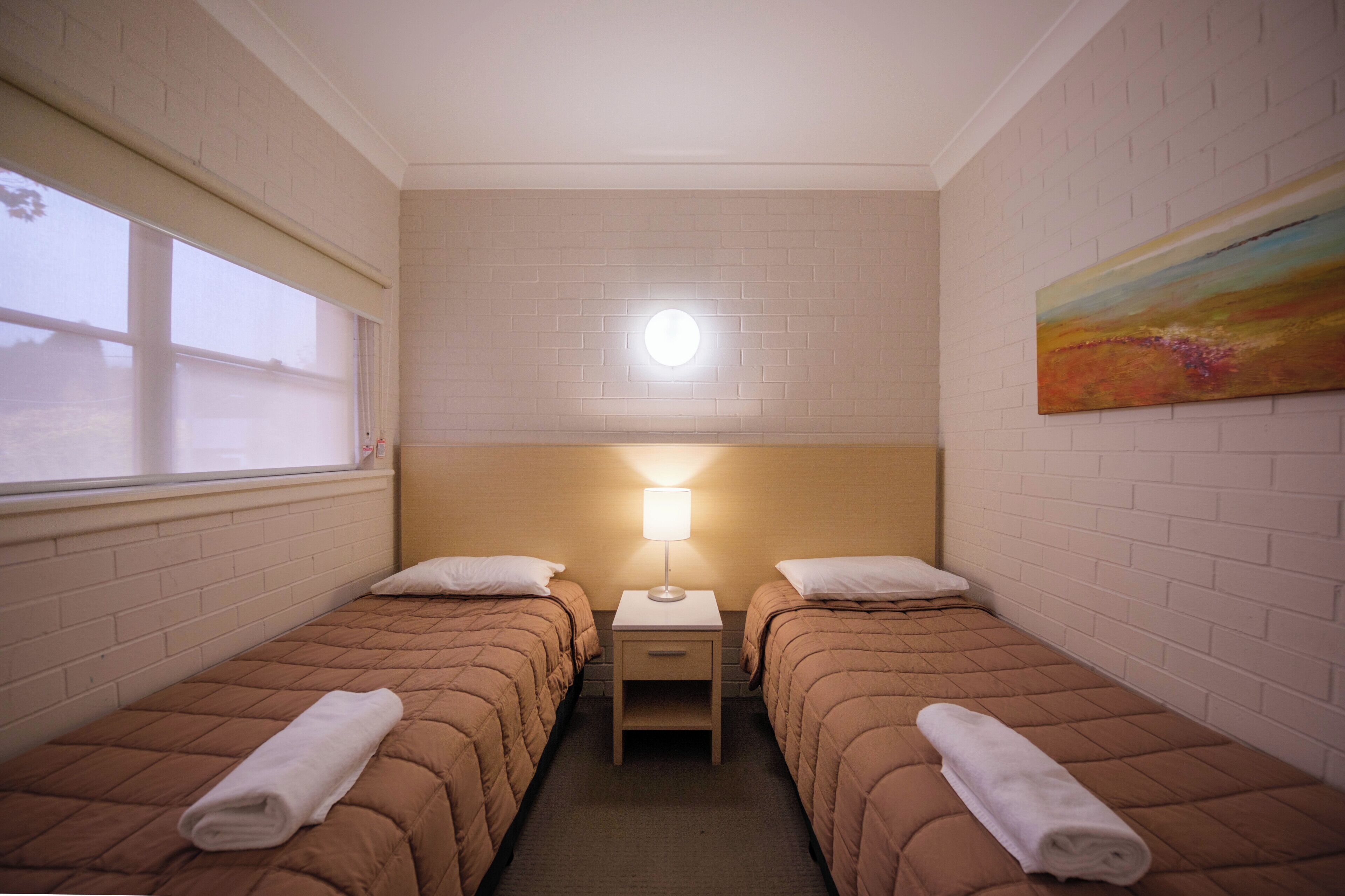 A twin room with two beds, a nightstand, a lamp, and a painting on the wall.