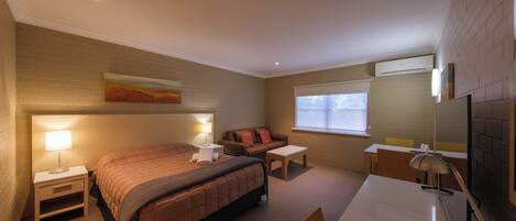 A hotel room with a bed, bedside tables, a desk, a chair, a TV, and a window with blinds.