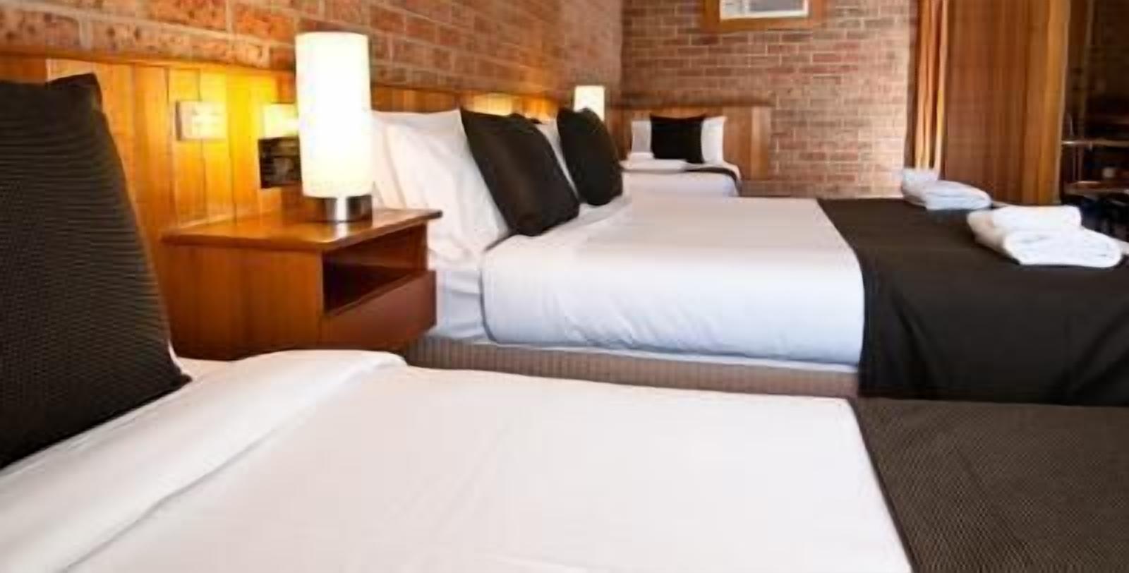 A hotel room with two beds, wooden headboards, and a brick wall.