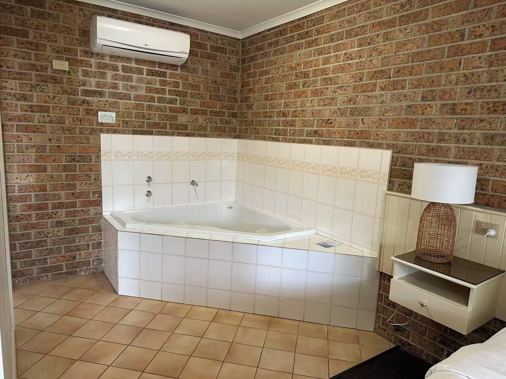 Un baño con bañera, un lavamanos blanco, un espejo y un equipo de aire acondicionado en la pared.