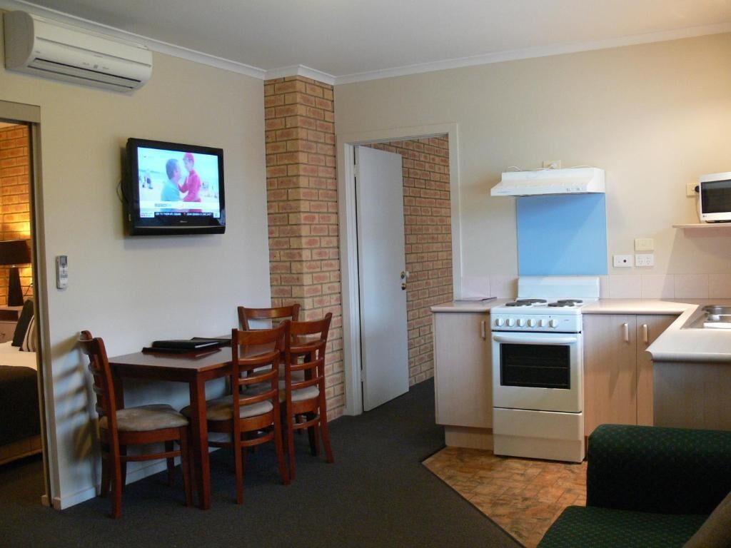 A compact living space with a dining area, a kitchen with a stove, and a television mounted on the wall.