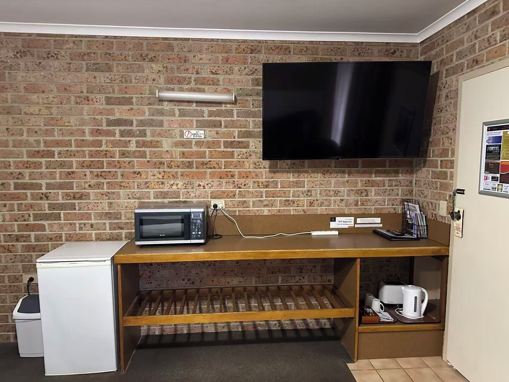 A compact room with a brick wall, a flat-screen TV, a microwave, a small refrigerator, and a coffee maker.
