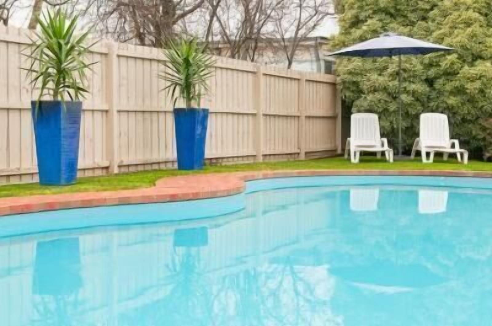 A swimming pool with a wooden fence and two potted plants.