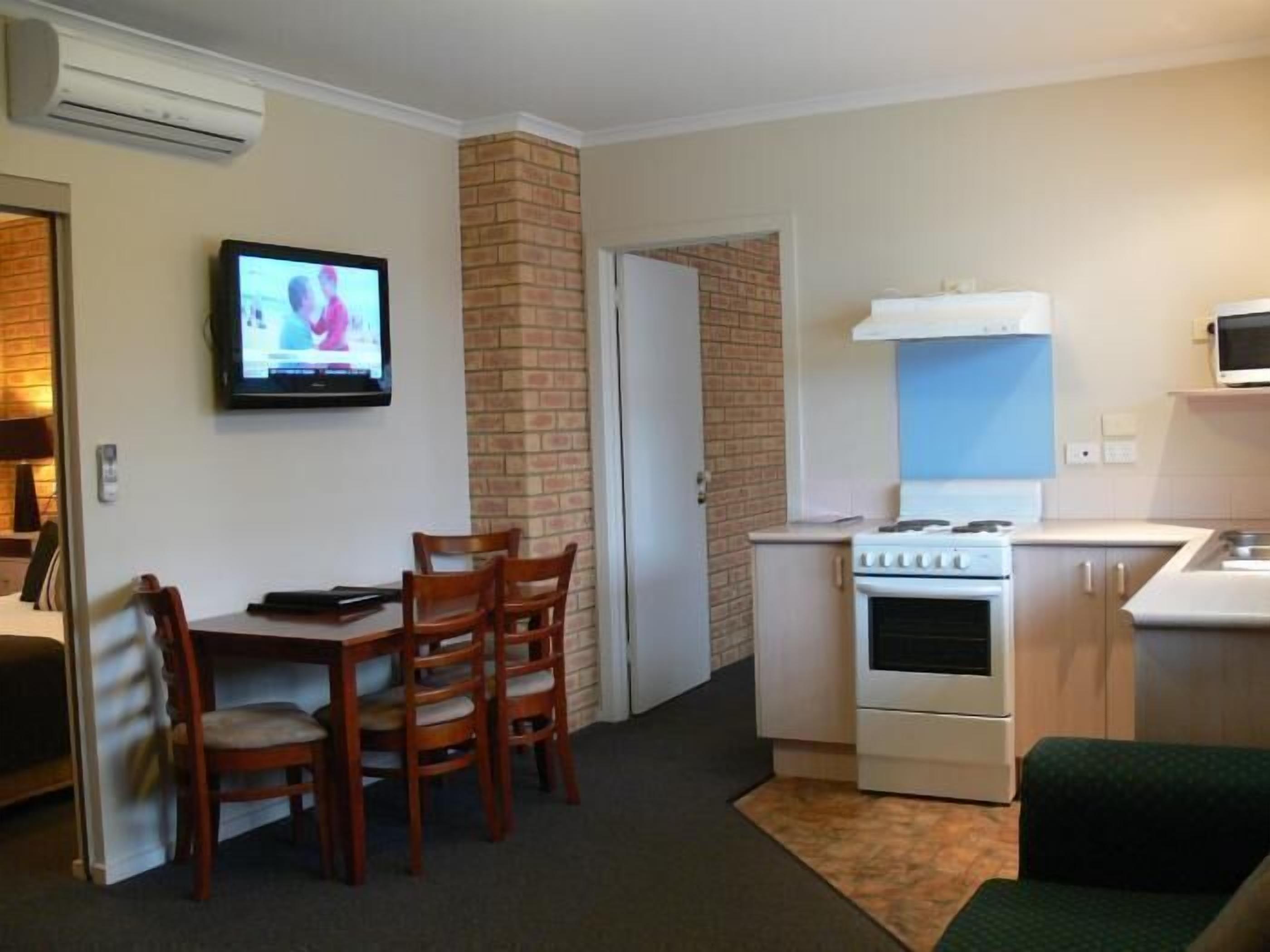 Un espacio habitable compacto con comedor, cocina equipada con estufa y microondas, y un televisor montado en la pared.