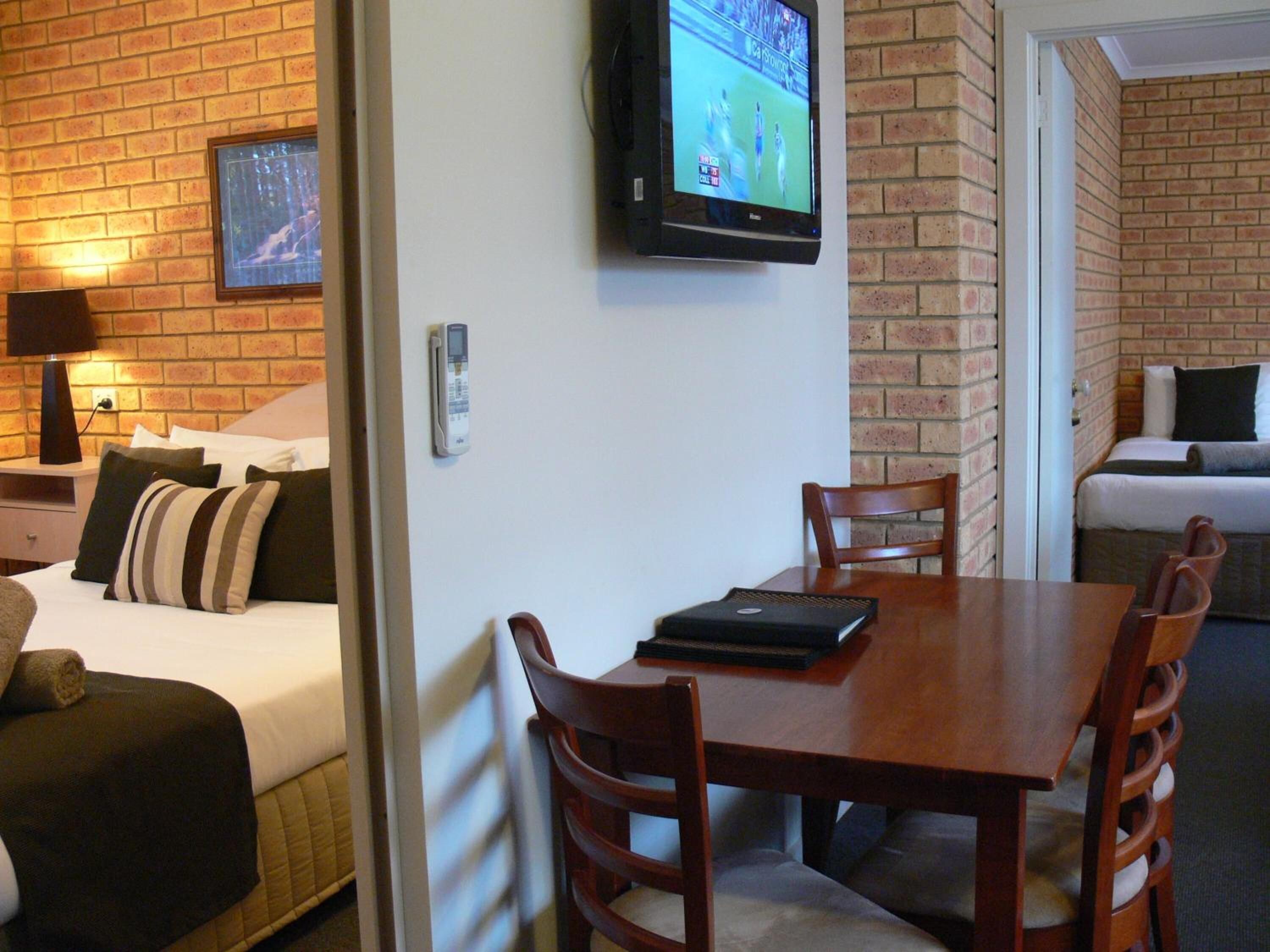 Een hotelkamer met een bakstenen muur, een bed met kussens, een aan de muur bevestigde televisie, een bureau met een laptop en een stoel.