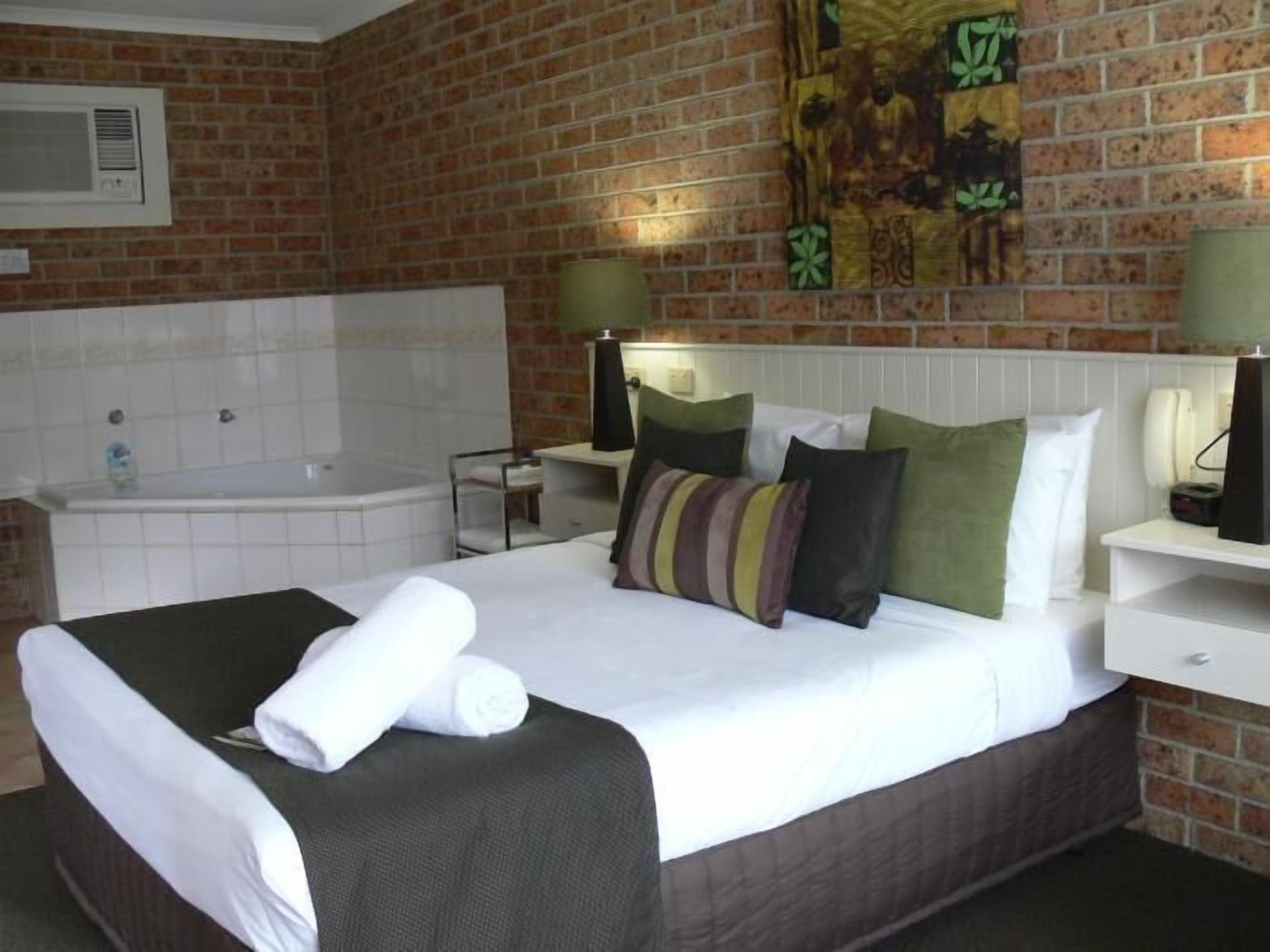 Une chambre d’hôtel avec un mur en briques, un grand lit avec du linge de lit blanc, une baignoire et un tableau accroché au mur.