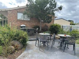 Un patio al aire libre con mesas y sillas redondas, rodeado de plantas y un edificio de ladrillo.