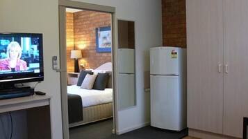 Quarto de hotel com televisão, cama, frigorífico e parede de tijolos.