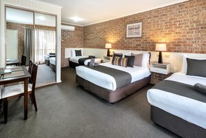 Una habitación de hotel con pared de ladrillo, dos camas, un escritorio y una silla.